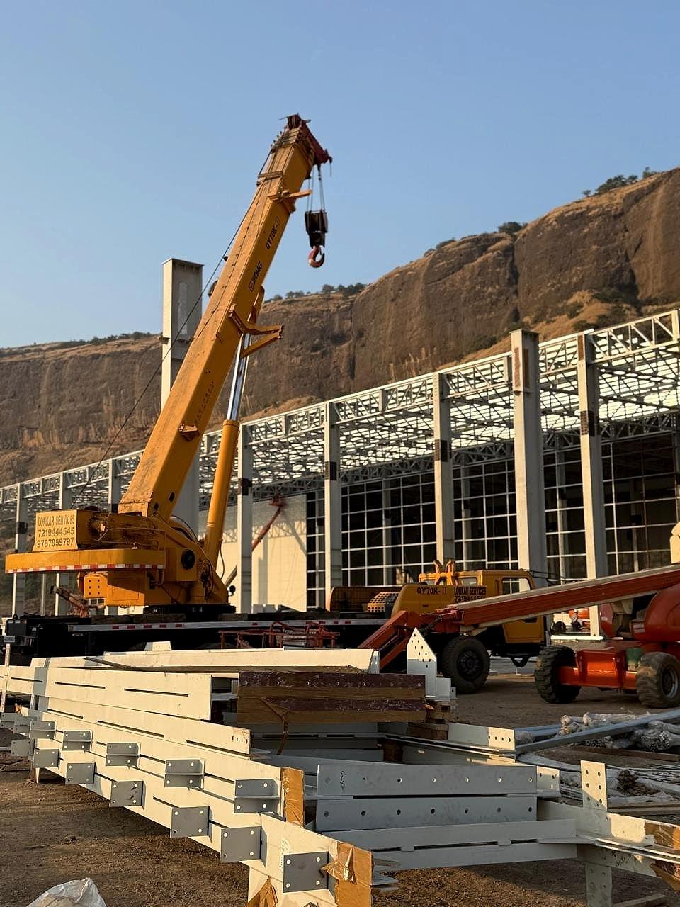 Mobile crane lifting a roof truss beside the glazed facade of the Hyundai plant structure, Pune